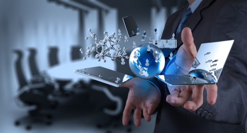 A person in a suit holds a holographic display of technology symbols, including a molecule, globe, and electronic devices, against a blurred conference room background.